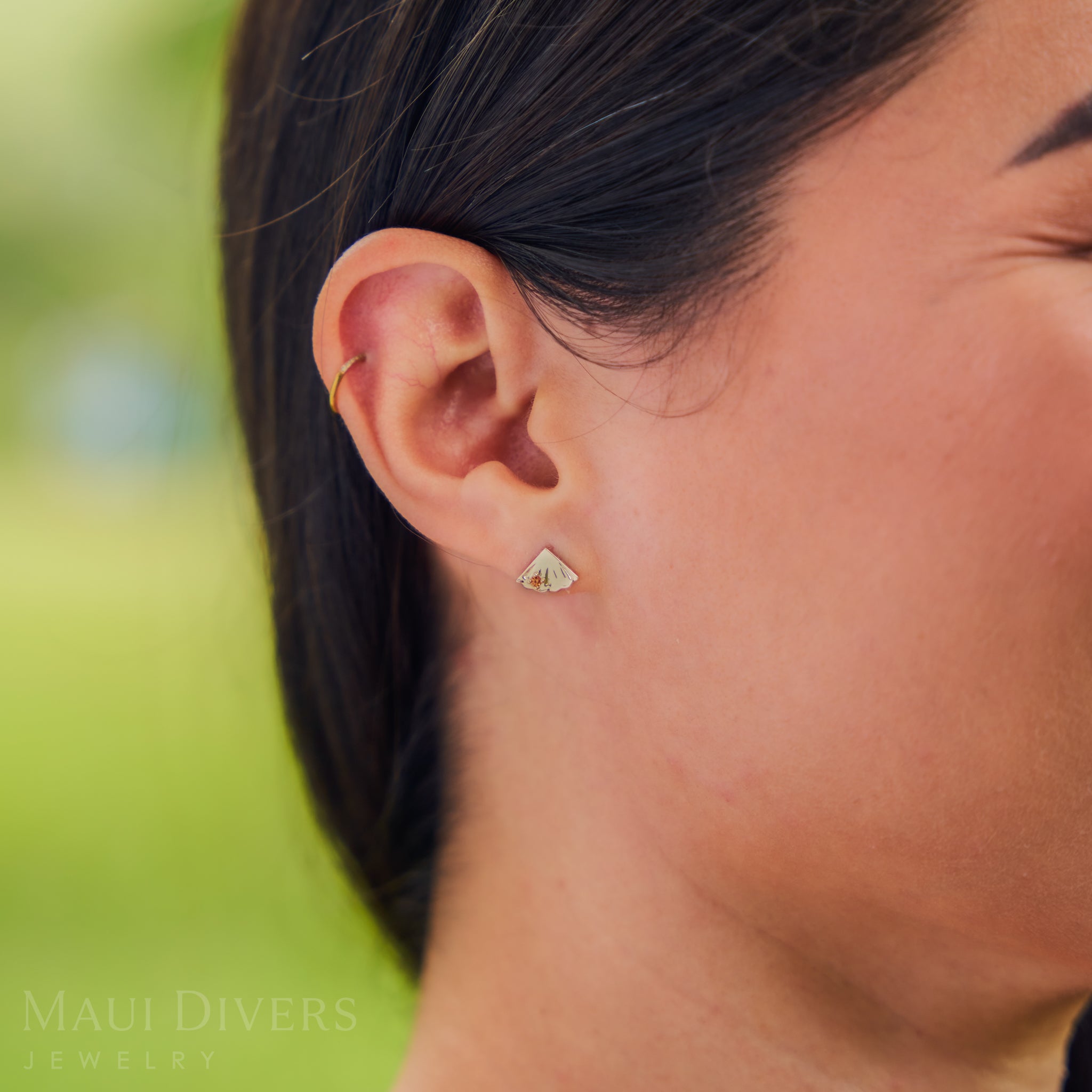 Close-up of an ear wearing a small pineapple earring with a blurred green background