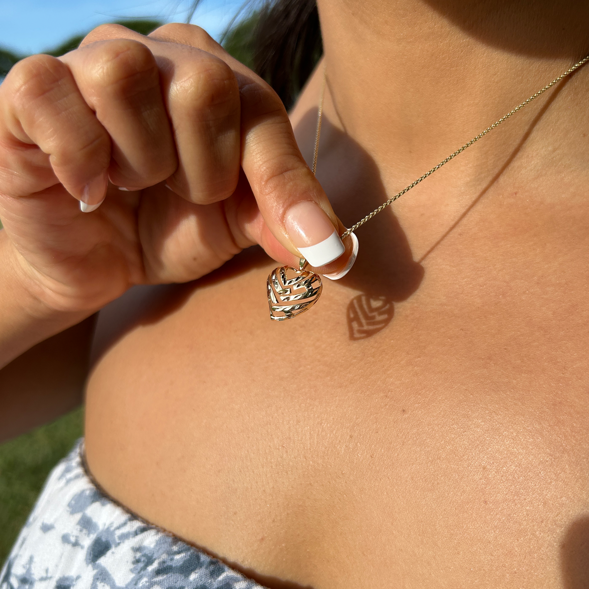 A woman holding an Aloha Heart Pendant in 14k Yellow Gold to show shadow that spells "Aloha"