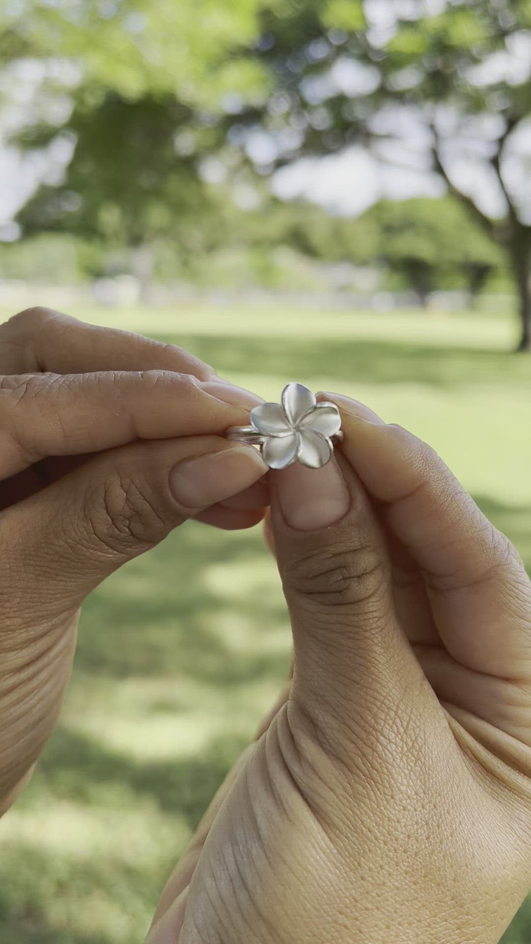 Video of a woman's hand holding a Plumeria Ring in Sterling Silver - 15mm by Maui Divers Jewelry and a bracelet.