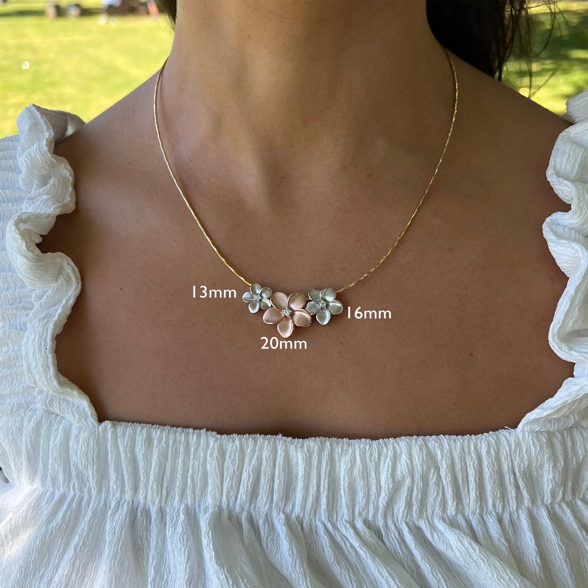 White Gold Plumeria Pendant & Rose Gold Plumeria Pendant on Model with Grassy Background with Scaling