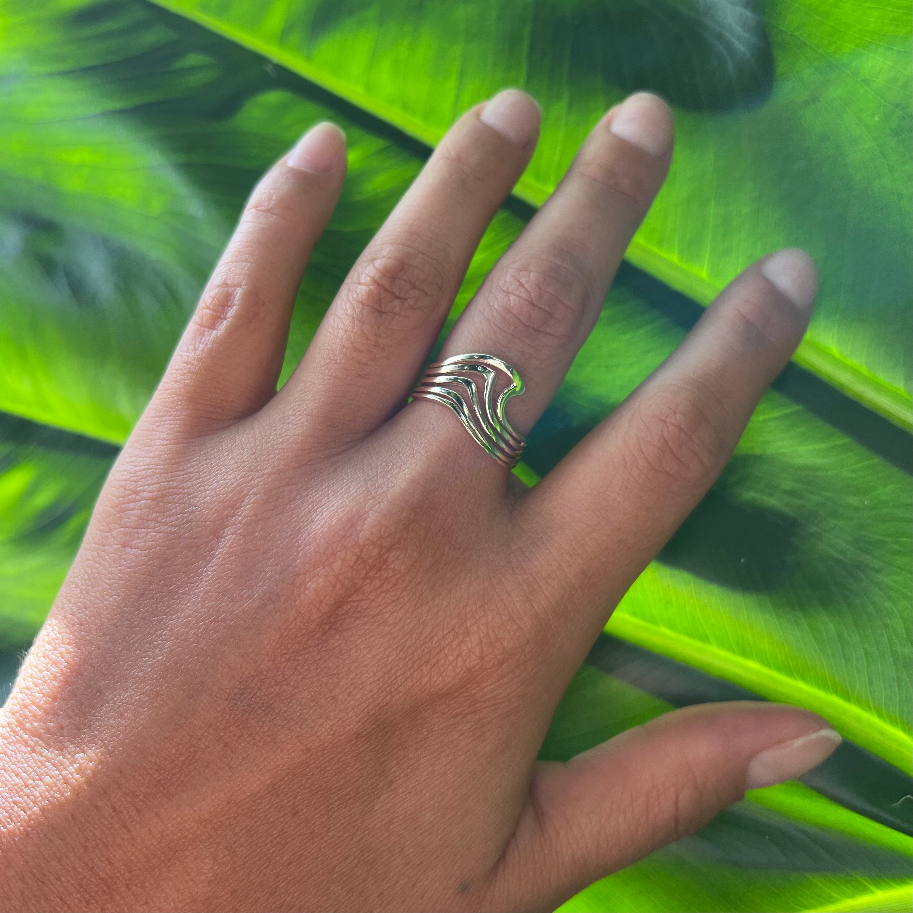 A woman's hand wearing an Abstract Nalu Ring in Gold on a leaf background