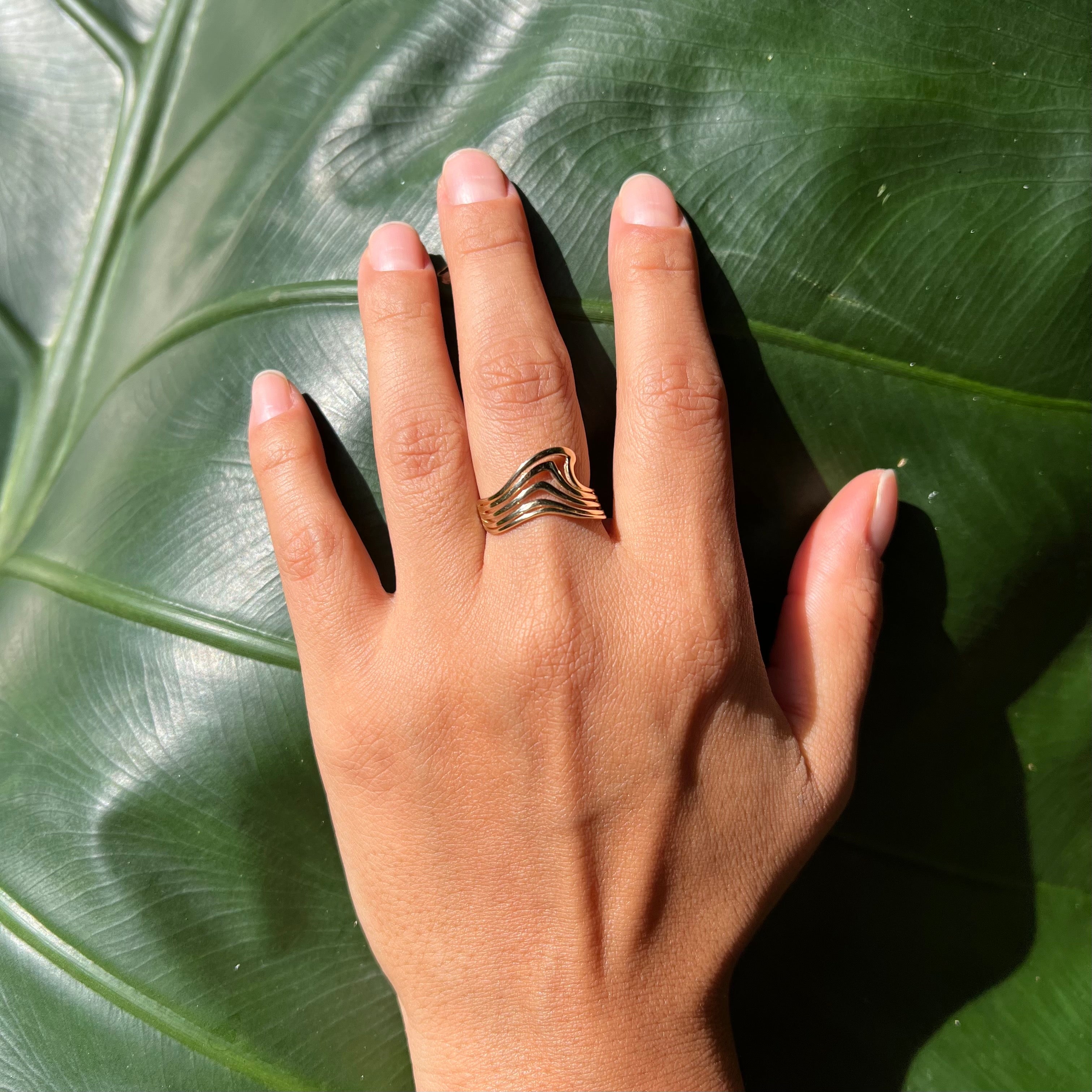 A woman's hand wearing an Abstract Nalu Ring in Gold on a leaf background