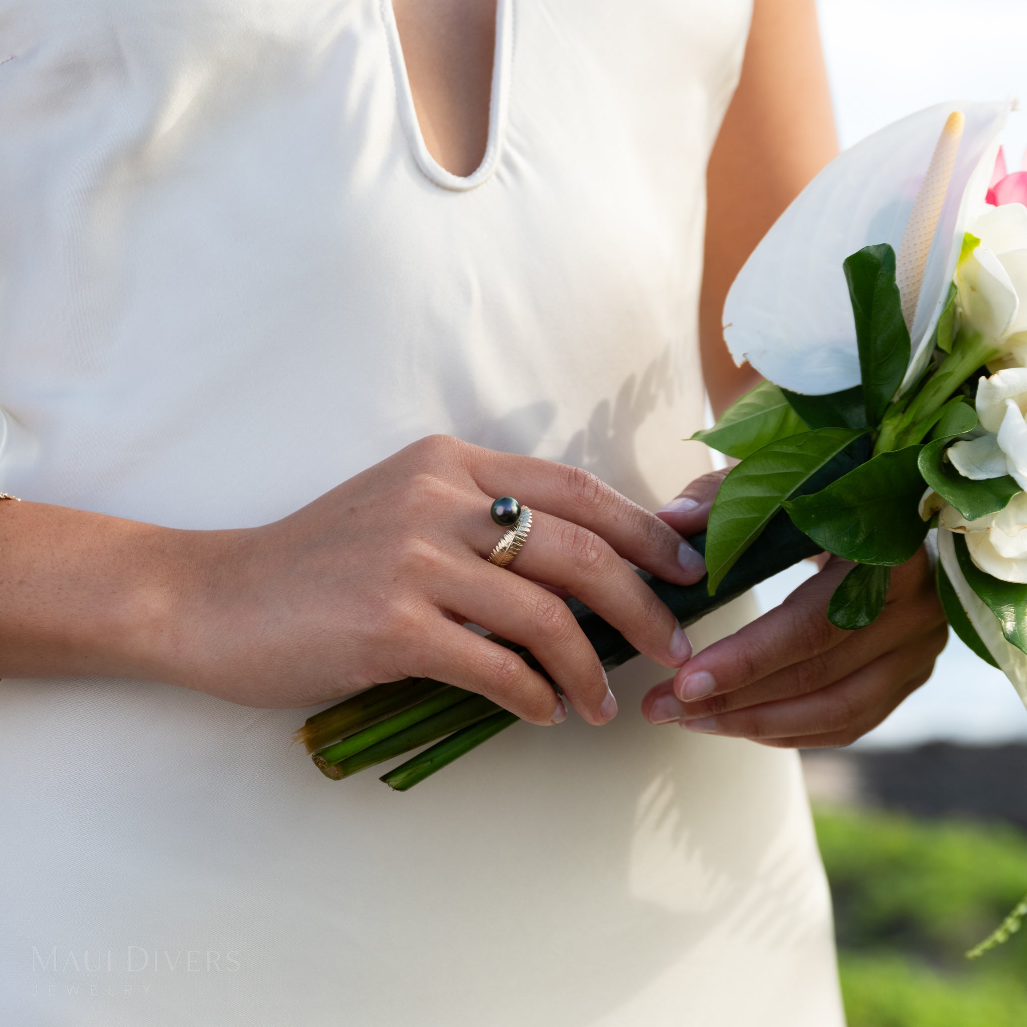 Close-up of a hand wearing the gold Kupukupu Fern Tahitian Black Pearl Ring and holding a bouquet 