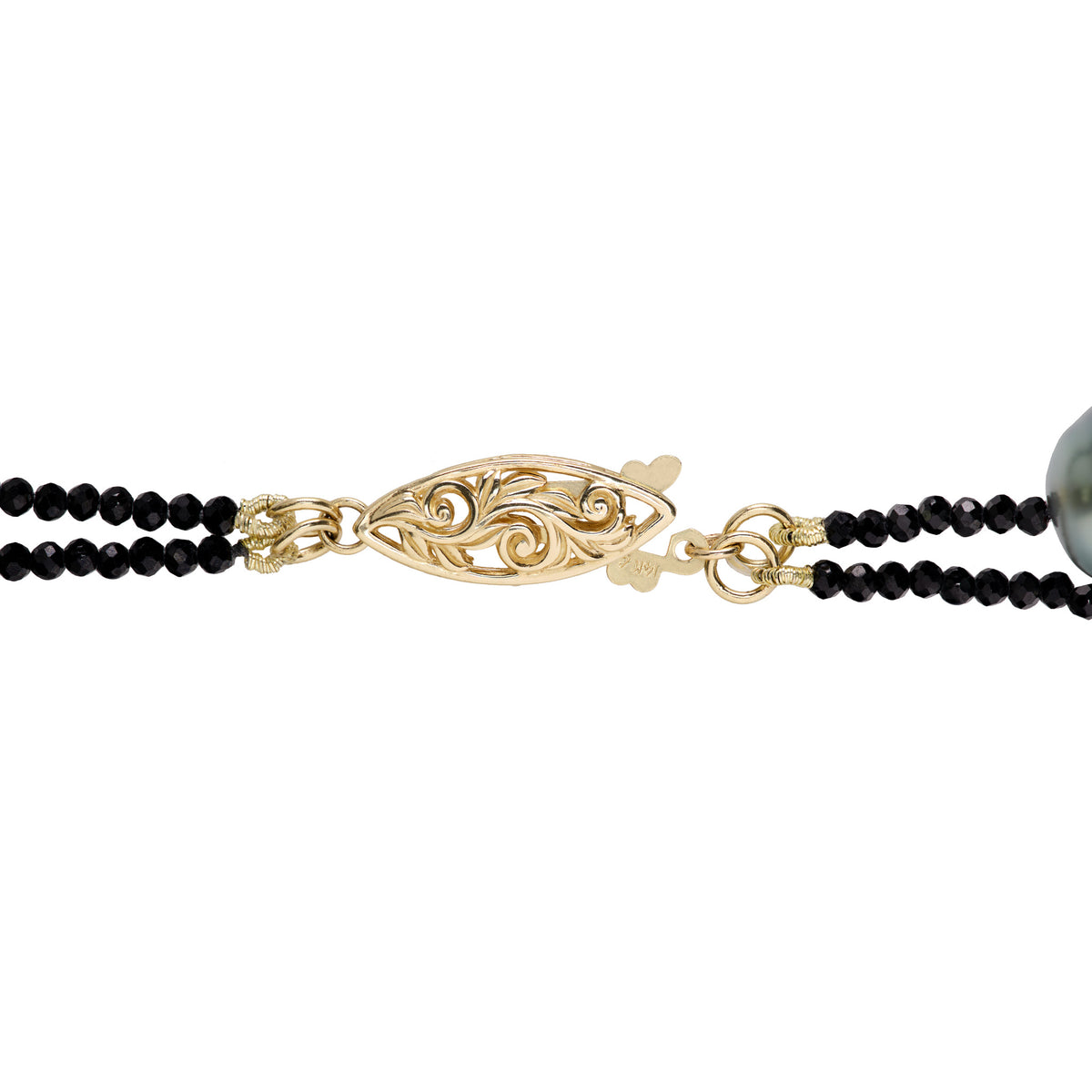 Detail shot of a football clasp in 14k yellow gold with filigree design and black spinel and a Tahitian pearl, shown on a white background