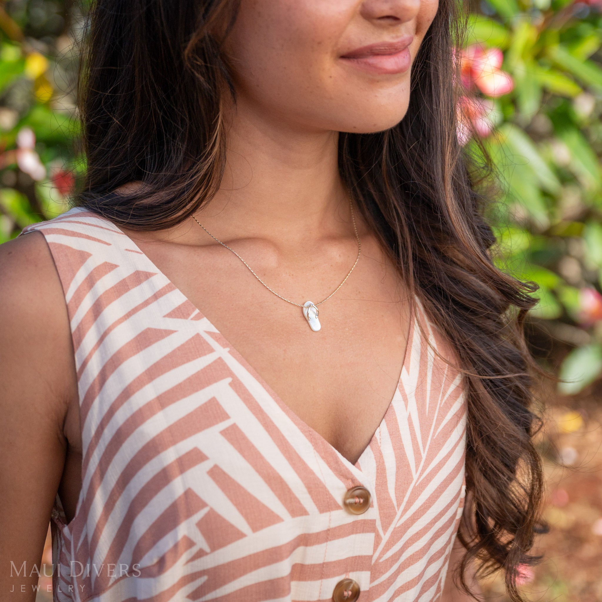 Woman wearing a White Mother of Pearl Slipper Pendant with 14k Gold details with a pink and green nature background. 