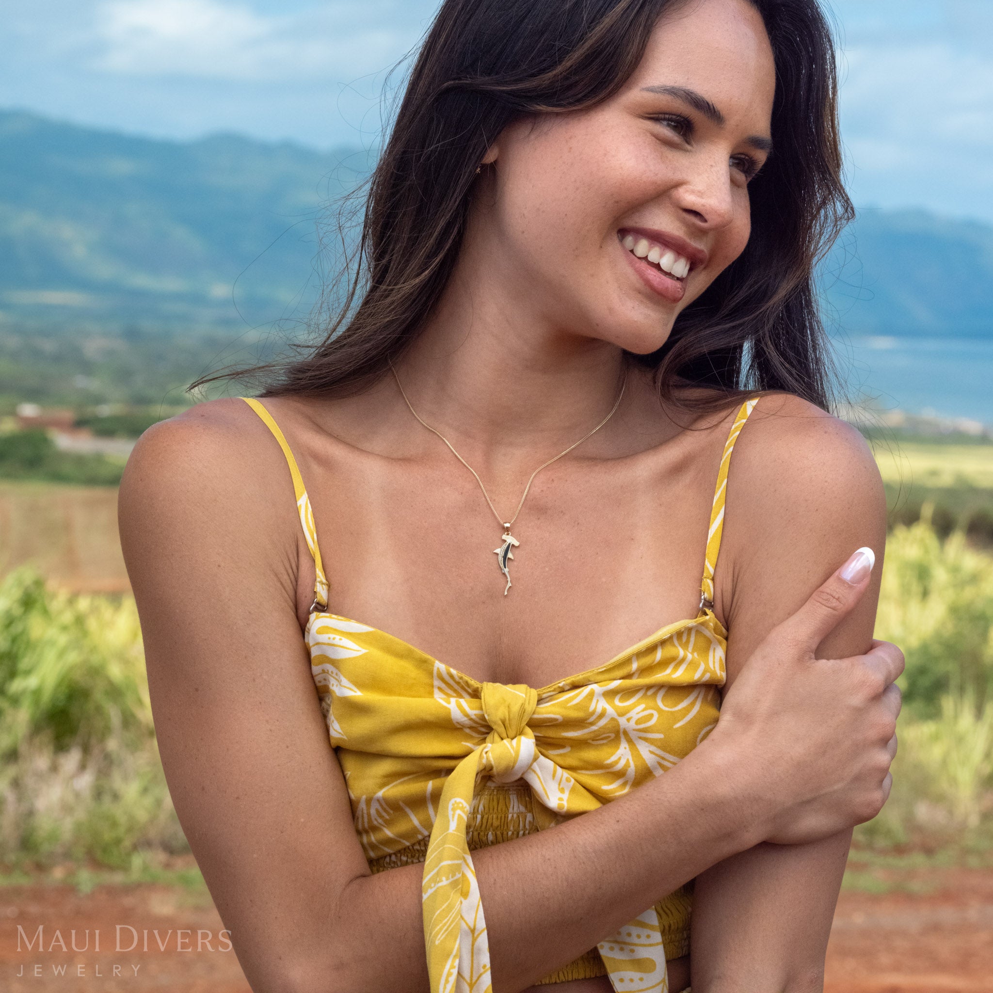 Woman smiling looking to the side wearing a 14k Gold Hammerhead Necklace with rare Black Coral and Natural Diamonds with green mountains blurred in the background.