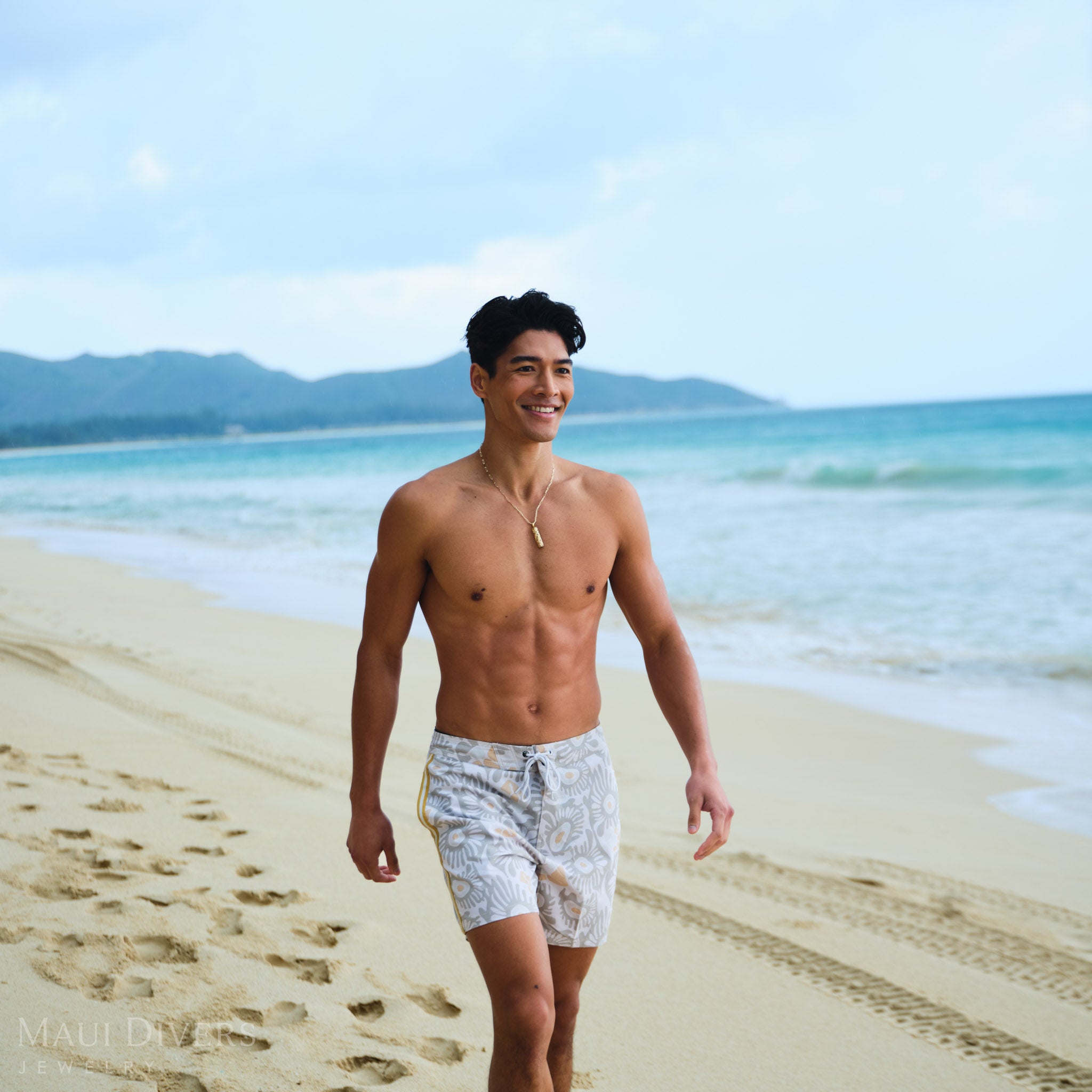 Man wearing a Hawaiian Heirloom Plumeria Pendant in Gold on a Paperclip Chain on a beach