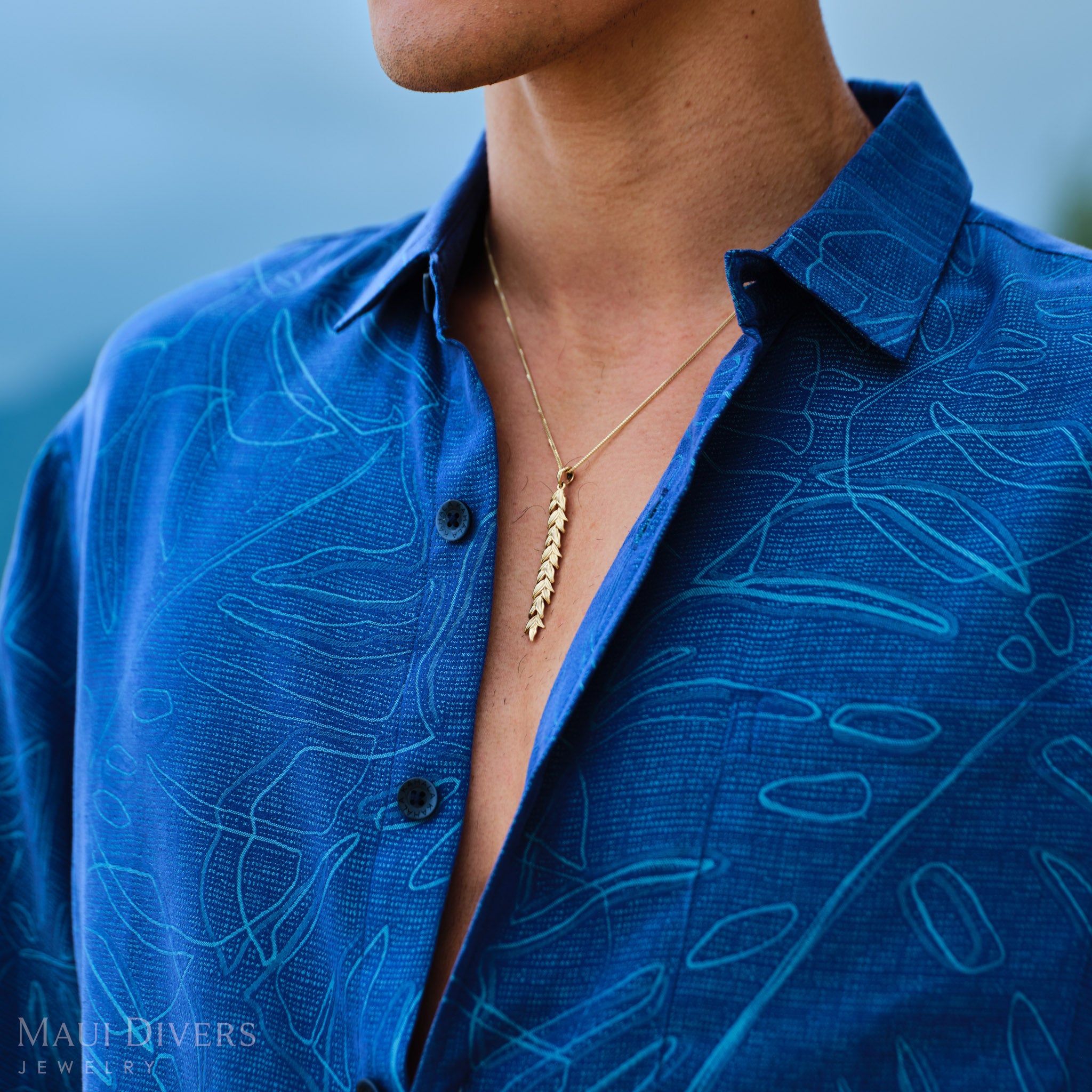 Man wearing a blue patterned shirt with a 58mm Maile Pendant in Gold outdoors
