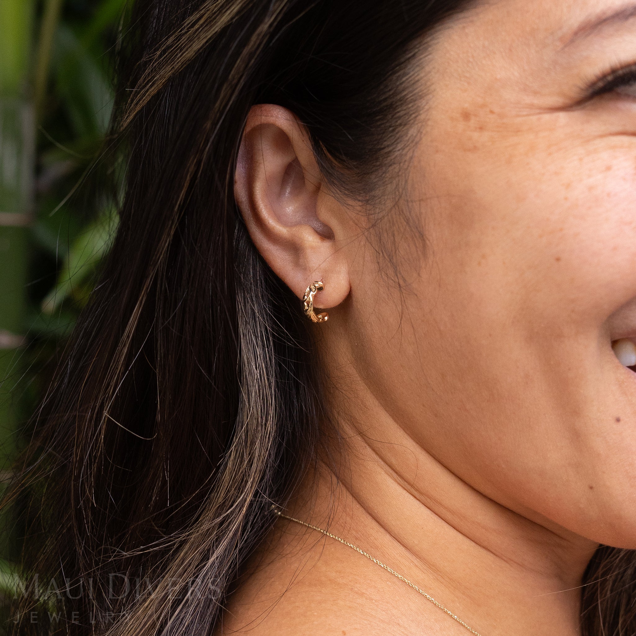 Close-up of a smiling woman wearing a Hawaiian Heirloom Old English Scroll Earrings in 14k yellow gold on her ear