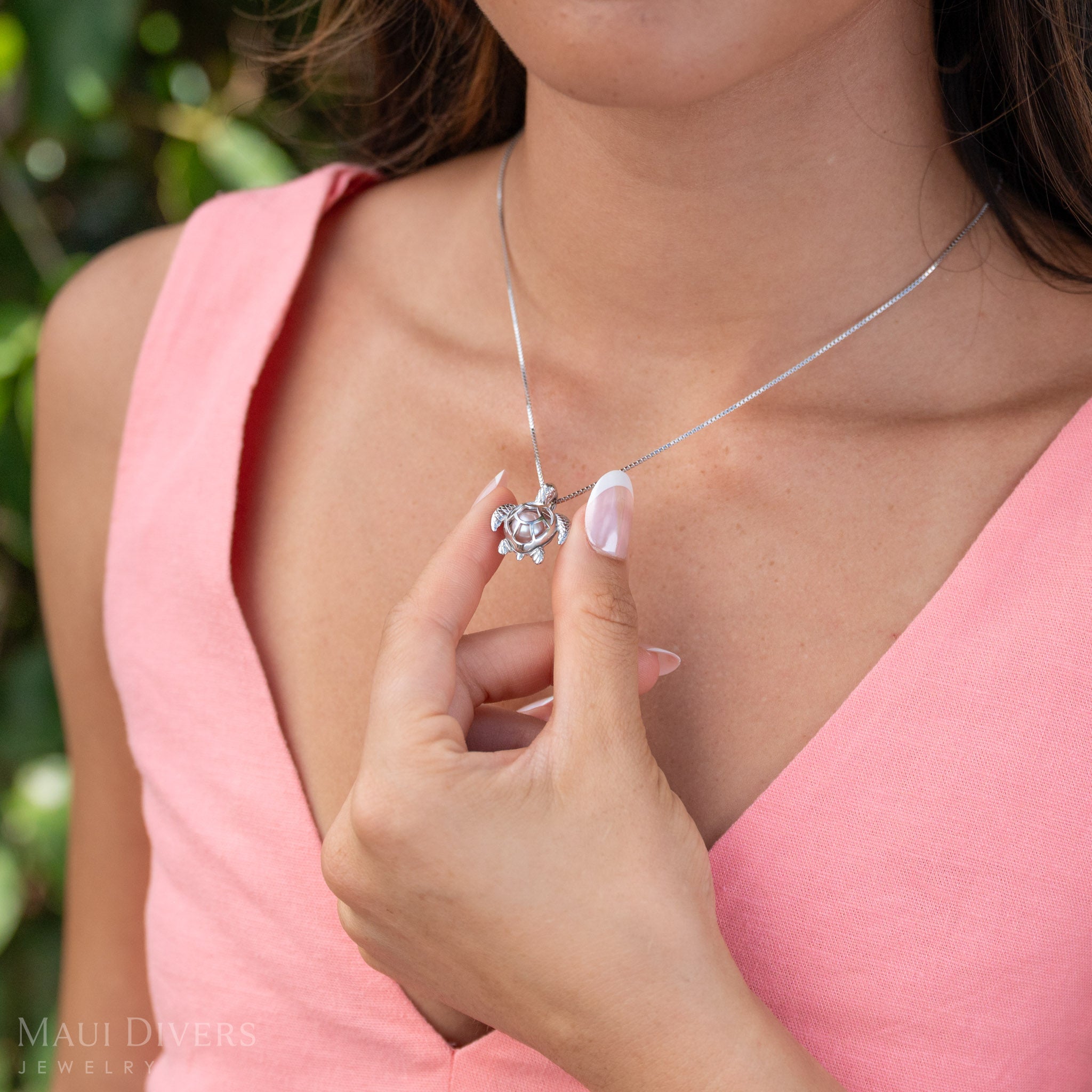 Woman wearing Pick A Pearl Honu Pendant in Sterling Silver with a Pink Freshwater Pearl, holding the turtle between her fingers. 