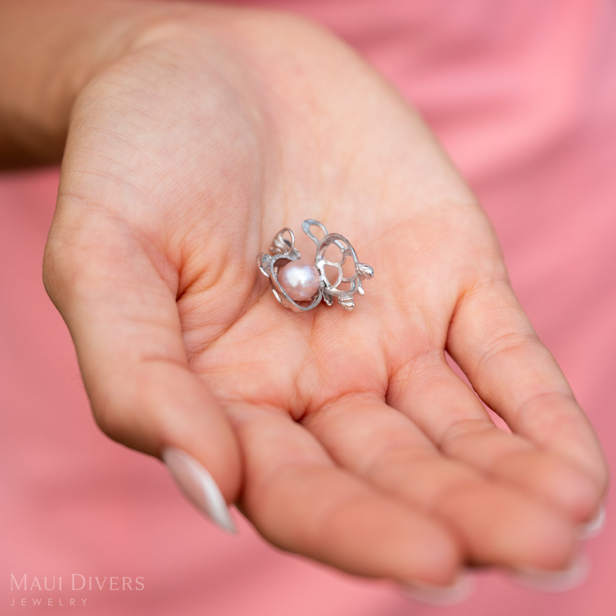 A Pearl Honu Pendant in Sterling Silver with a Natural Pink Freshwater Pearl in a woman's hand with the case opened to reveal the pearl. 