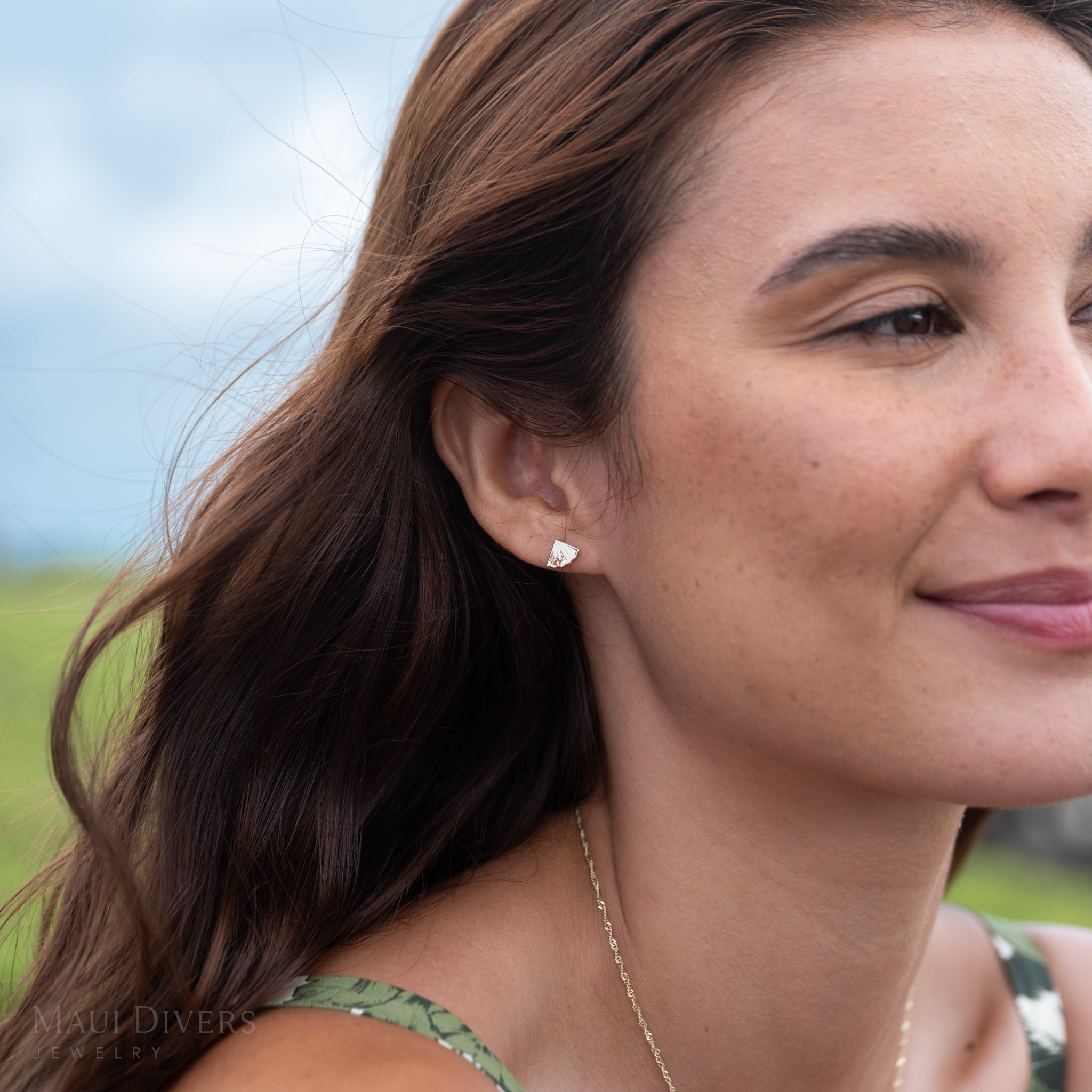 Woman wearing a gold and orange sapphire pineapple slice earring with a blurred natural background