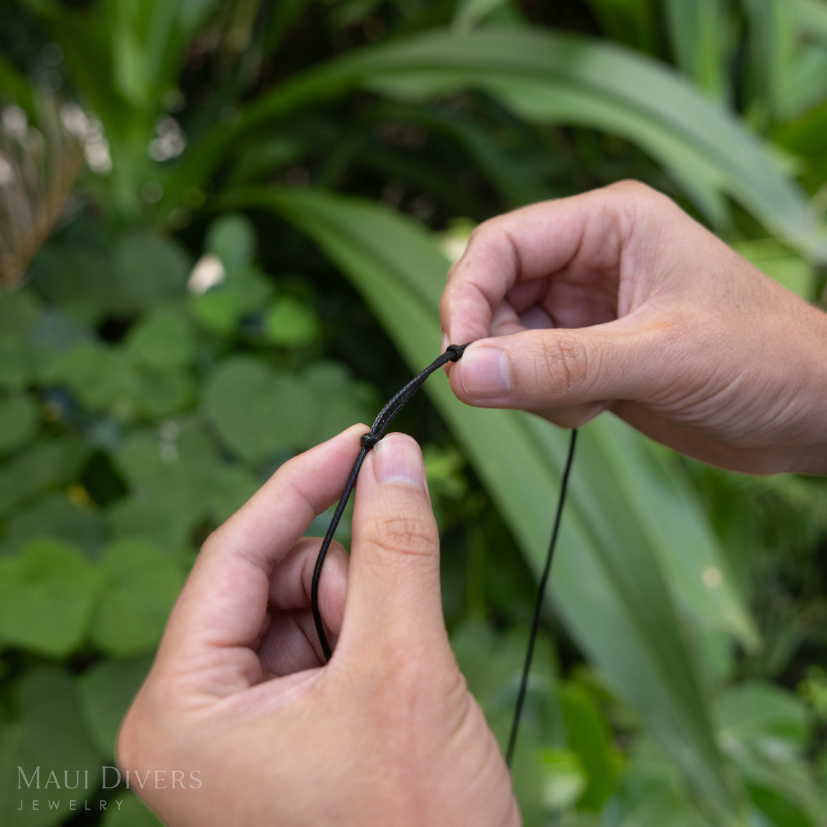 Hands showcasing the black cord fastener of a necklace against a blurry nature background