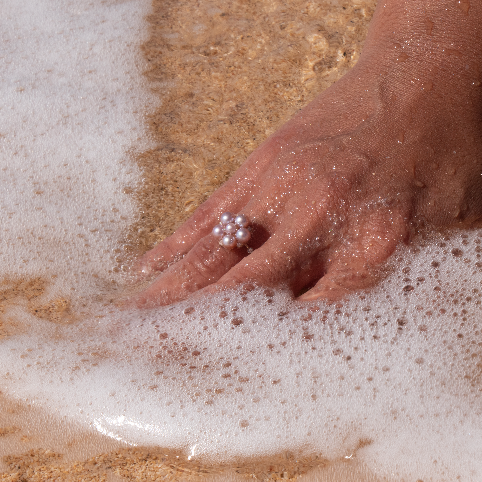 A woman's hand in the sand wearing a Tiny Bubbles Lavender Freshwater Pearl Ring in Gold with Diamonds - Maui Divers Jewelry